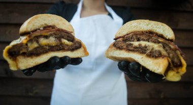 Ahşap desenli bir duvarın arka planında sulu bir burger tutan bir şefin yakın plan fotoğrafı..