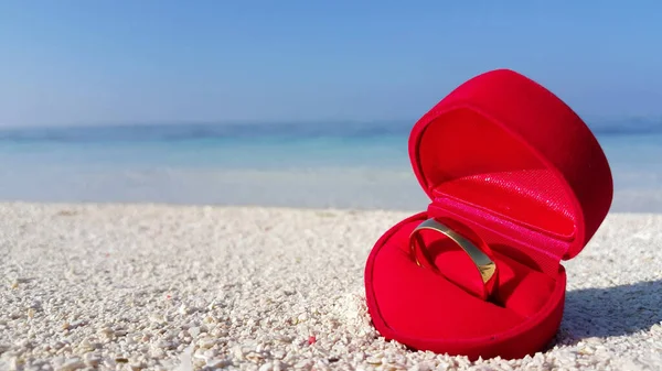 Κοντινό Πλάνο Δαχτυλιδιού Κόκκινο Κουτί Αμμώδη Παραλία Πάνω Γαλαζοπράσινη Θάλασσα — Φωτογραφία Αρχείου