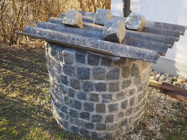 A photo of a stone well with a zinc board and stones on top