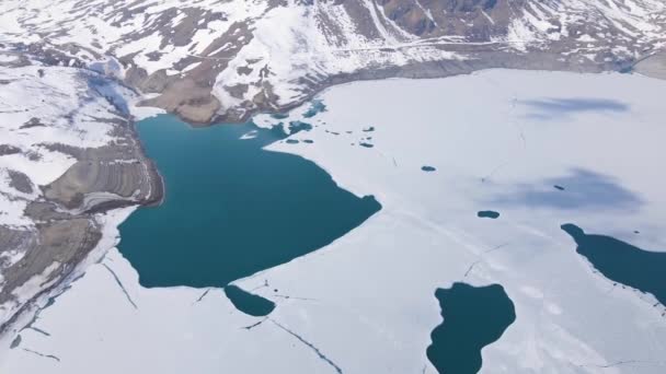 岩だらけの雪の山に囲まれた凍るような山の湖の空中写真 — ストック動画