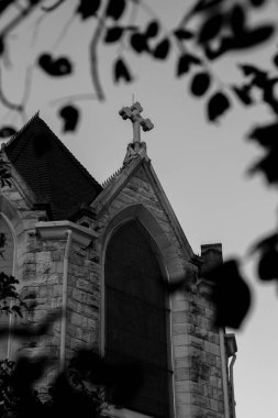 Bulutlu gökyüzüne karşı kilise çan kulesinde bir taş haçın düşük açılı gri görüntüsü.