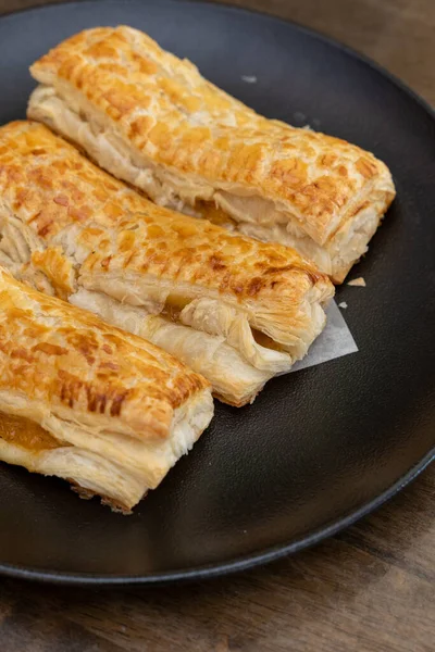 A baked puff pastry with toppings on a black plate