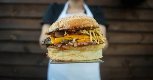 Zbliżenie Ujęcia Kucharza Trzymającego Soczystego Burgera Tle Drewnianej Teksturowanej Ściany — Zdjęcie stockowe