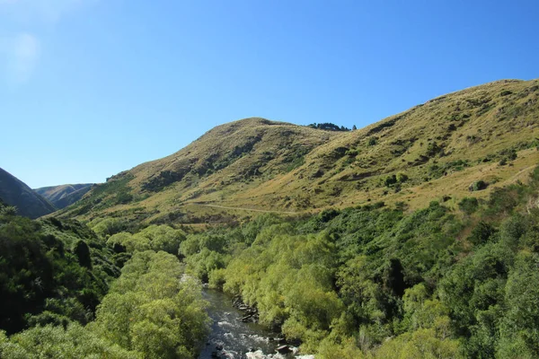 ニュージーランドのオタゴの湖に対する低木で覆われた丘を流れる川の景色 — ストック写真