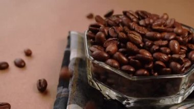 Kahve çekirdekleri yakın plan çekimde pembe arka planda cam bir kaseye düşüyor.