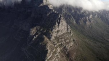 Cape Town Sinyal Tepesi uçurumunun mavi gökyüzü arka planıyla bulutlara ulaşan insansız hava aracı görüntüsü.