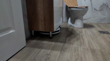 Modern bir banyonun zeminini temizleyen beyaz robot süpürgesi.