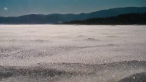 山を背景に 風に吹かれながら地面に降る雪の景色 — ストック動画