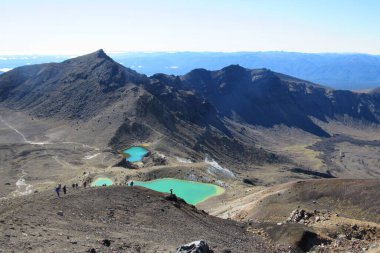 Tongariro Ulusal Parkı, Yeni Zelanda 'da kayalık tepelerde çalılarla kaplı bir göl manzarası.