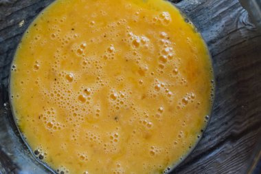 Bir cam kase, piknik masasında, pişmeye hazır parlak sarı yumurtalarla.