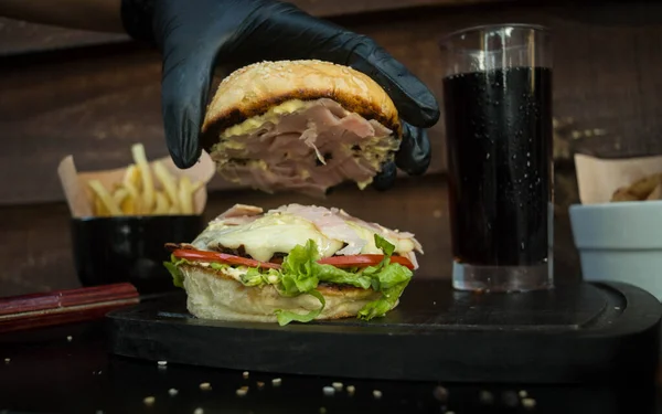 Närbild Hand Som Håller Hamburgerbulle Bredvid Ett Glas Dryck Mörk — Stockfoto