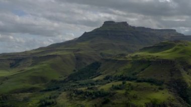 Mavi bulutlu arka planda yemyeşil dağlarla dolu bir manzaranın havadan görüntüsü.