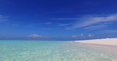 Güneşli bir günde, turkuaz bir denize karşı kumlu bir sahilin manzarası.