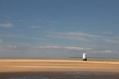 Kumlu sahilde, dalgaların çekildiği beyaz bir kule.