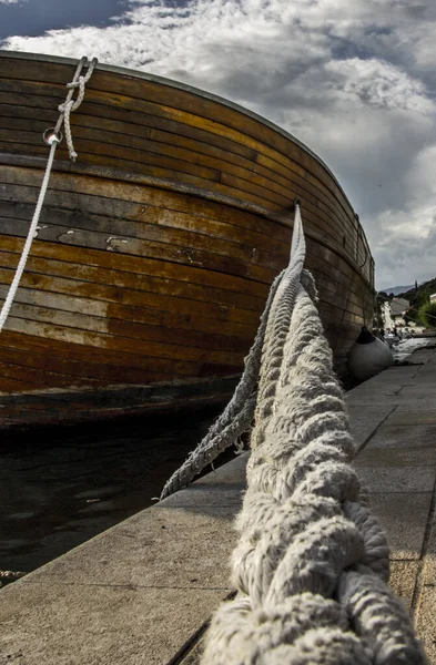 A low angle of a rope and a wooden boat against a cloudy sky