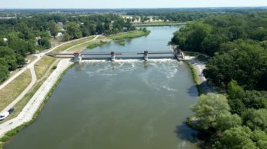 Nehrin kenarlarında ağaçlar ve nehirde bir baraj sistemi olan bir nehir manzarası.
