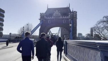 Londra 'daki Tower Bridge manzarası, yürüyen insanlarla ve güneşli bir günde geçen arabalarla dolu.