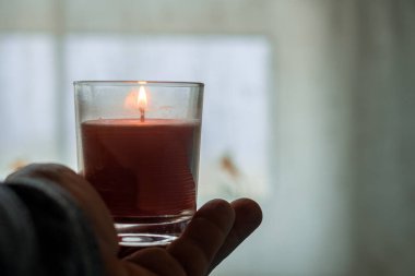 İnsan avucundaki şeffaf camda yanan bir mum.