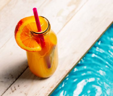 Bir fincan portakal suyu, portakal dilimi ve samanla dolu yüksek açılı bir poz.