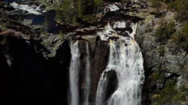 Şelalenin yanındaki kayada dinlenen bir kadın.