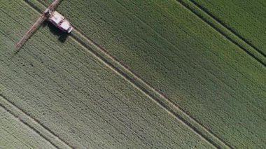 Yeşil bir tarlada sürüş yapan bir ekin püskürtücü arabanın havadan görünüşü.