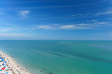 Kıyıdaki kumlu kumsalın hava manzarası bulutlu mavi gökyüzünün altında parlıyor.