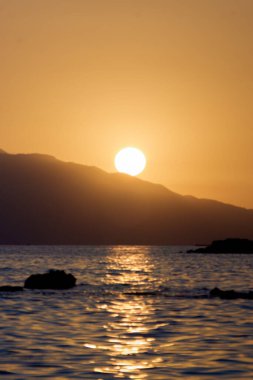 Tepenin arkasında batan güneş ve denizin dikey görüntüsü..