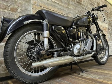 Duvarın önüne park etmiş siyah bir motosikletin yakın çekimi.