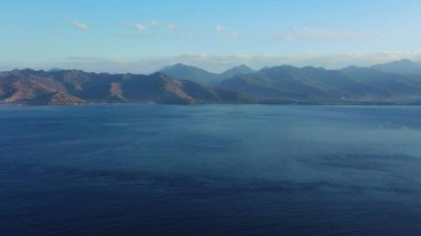Mavi gökyüzü ve arka planda dağlar olan mavi bir deniz manzarası.