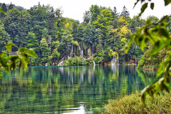 环绕着茂密绿树的瀑布映衬下的小城湖景 — 图库照片