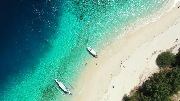 An aerial drone shot of a sandy beach with two boats washed by the Indian Ocean