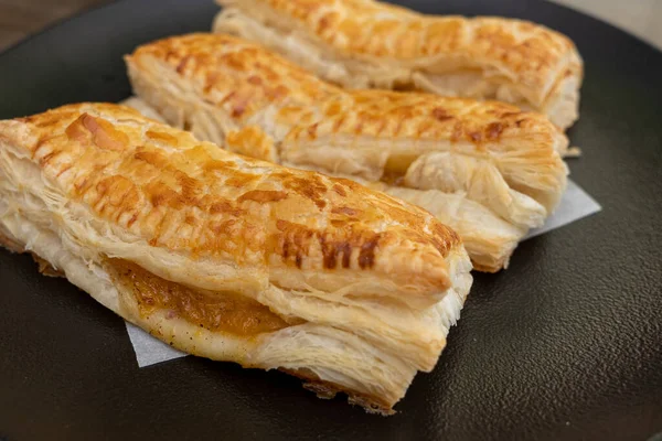 A baked puff pastry with toppings on a black plate