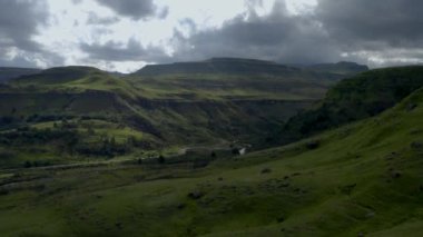 Koyu bulutlu bir arka planda yemyeşil dağlarla dolu bir manzaranın havadan görüntüsü.