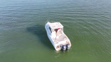 Durgun denizde yüzen beyaz bir teknenin havadan çekilmiş görüntüsü.