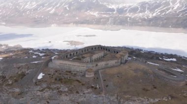 Dağlardaki donmuş göl ve barajın yanındaki antik kale kalıntılarının 4K hava aracı görüntüsü
