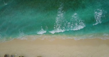 Güneşli bir günde, turkuaz bir denize karşı kumlu bir plajın havadan görünüşü.