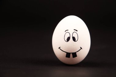 Siyah bir yüzeye komik bir yüz resmi çizen bir yumurtaya yakın plan.
