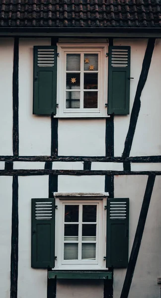 A vertical closeup of an old white building with green windows