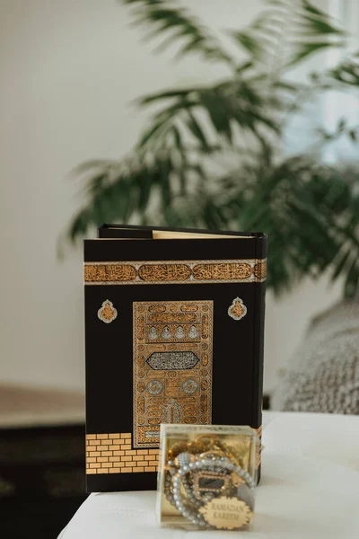 The prayer set-black rug and black velvet Quran, decorated with Kaaba pattern, and rosary made of beads with the inscription Ramadan Kareem