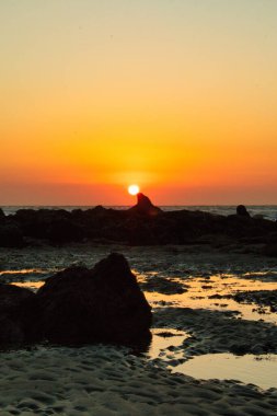 Deniz dalgalarının dikey görüntüsü, nefes kesici bir gün batımında kayalık kıyıya vuruyor.