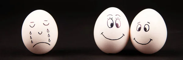 A closeup of happy and sad faces on white and brown eggs on a black surface