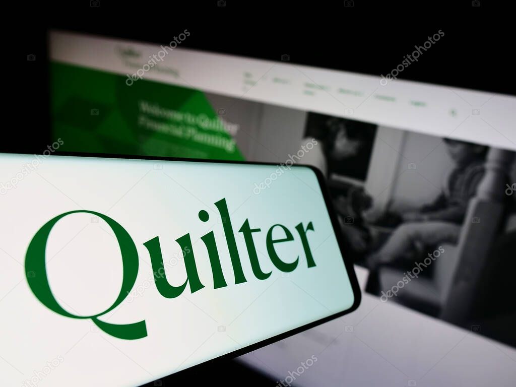 Mobile phone with logo of British wealth management company Quilter plc on screen in front of website. Focus on center-left of phone display.