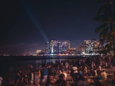 Hawaii, Waikiki 'de yeni yıl arifesinde arka planında aydınlık binalar olan insanlarla dolu bir sahil.