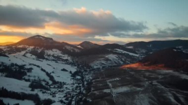 Gün batımında karla kaplı dağların doğal manzarasını gösteren bir drone görüntüsü.