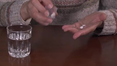 Yaşlı kadın ilaç şişesinden iki hap dolduruyor. Ağrı kesici kapsülleri var. Ağrıyı dindirmek için ilaç alıyor..