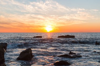 Güneşin güzel bir görüntüsü denize yansıyor. Kocaman kayalarla..