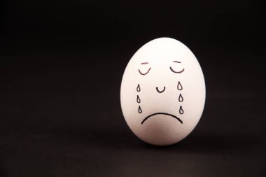 Siyah arka planda komik bir yüzü olan boyalı bir yumurtaya yakın plan.