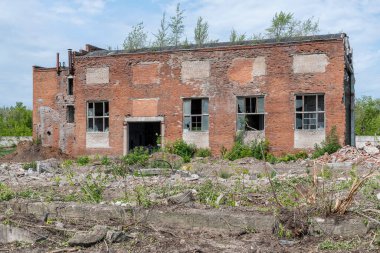 Kırmızı tuğladan yapılmış eski endüstriyel atölye, harap olmuş, kırık pencere ve kapılar ile mavi yaz gökyüzünün arka planında