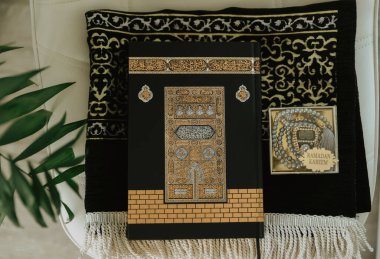 Kabe deseniyle süslenmiş siyah halıyla siyah kadife Kuran ve Ramazan Kareem yazılı tespih.