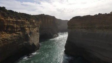 Su bulutlu bir gökyüzüne karşı büyük kayaların arasından akıyor.